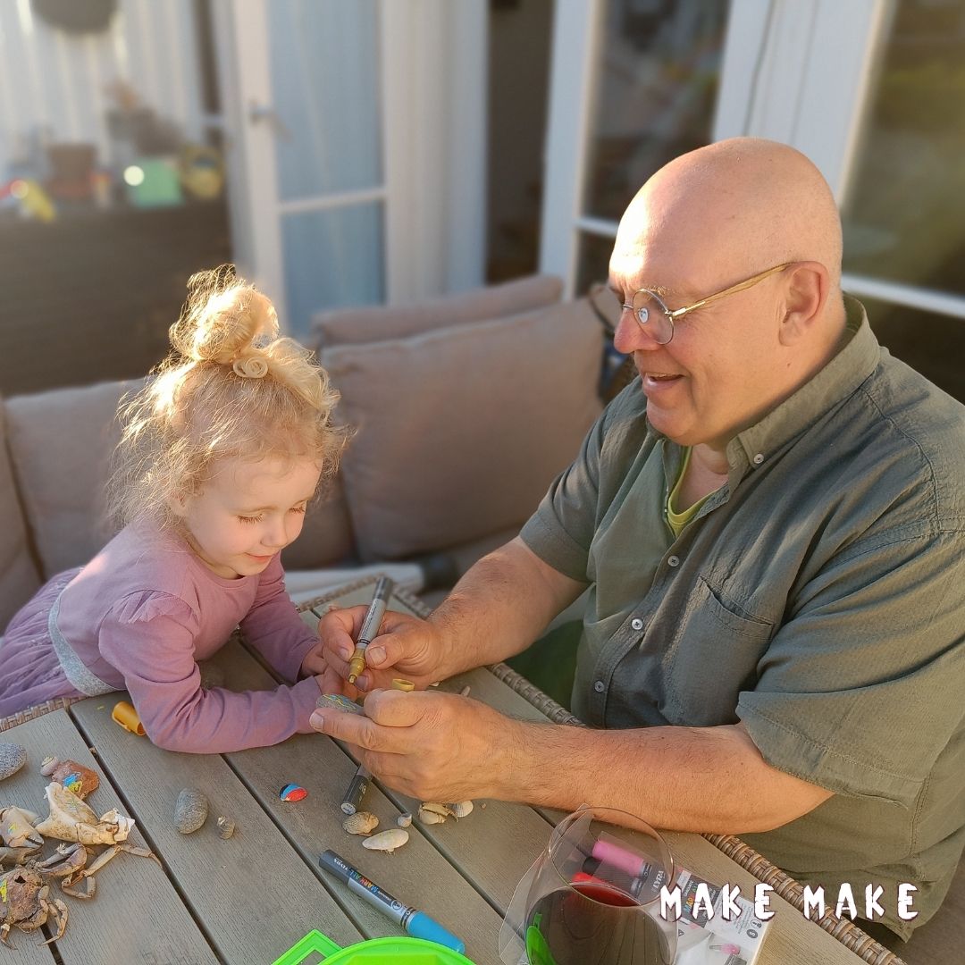 Bedstefar og barnebarn sidder og hygger med et kreativt projekt - de maler p sten de har fundet p stranden med graduate mark all tuscher. 