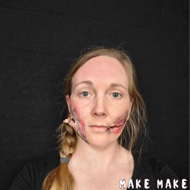 Kvinde med fake wounds lavet med flydende latex. P den ene kind hnger der store laser af hud, og p den anden kind er der lavet et cut fra mundvigen og op. 